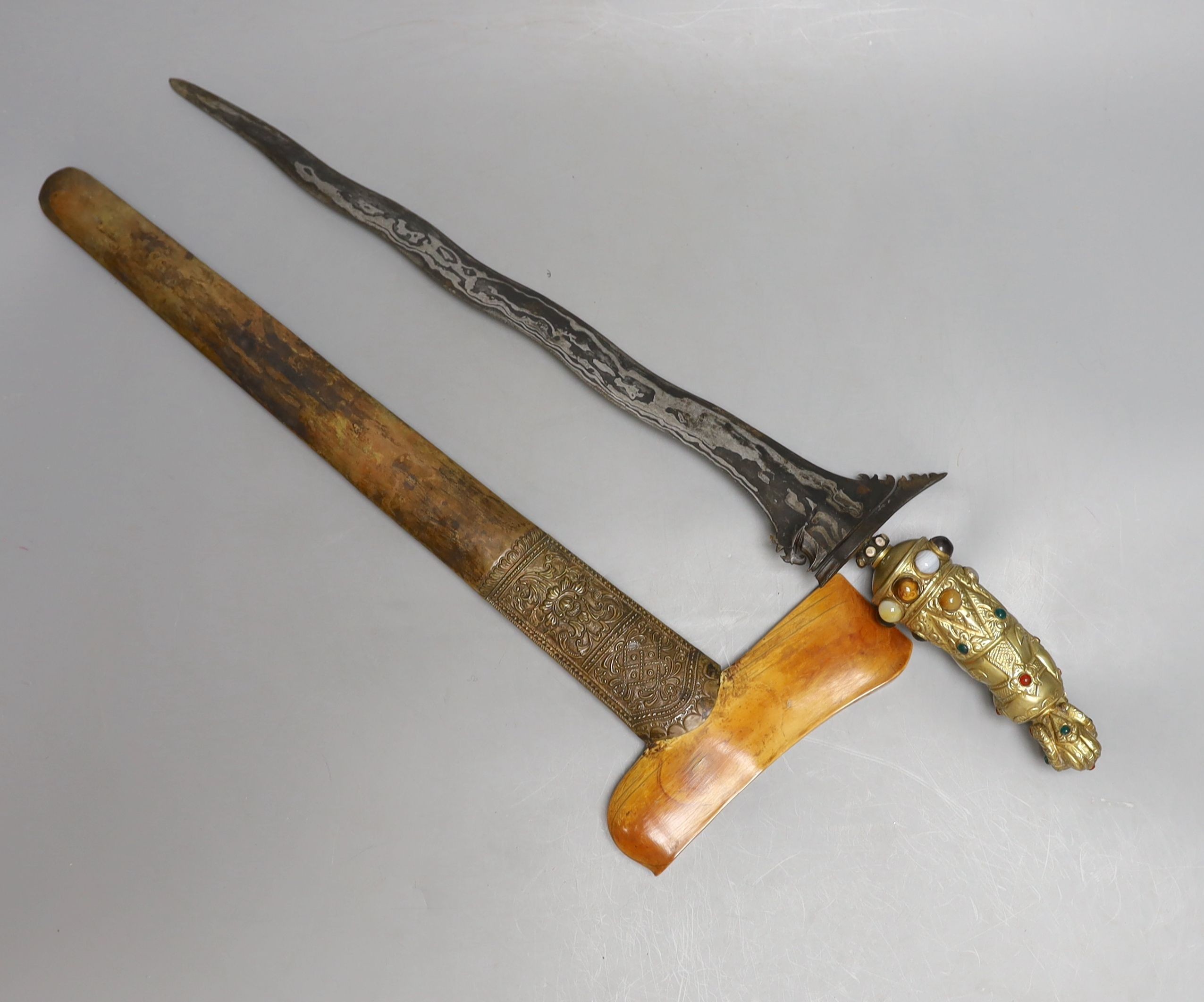 A Fine Balinese dagger kris, 19th century, earlier wavy pamor blade 43cms, later gilt brass figural handle set with cabochon stones and pastes, in its scabbard with embossed brass cover and earlier carved ivory top.